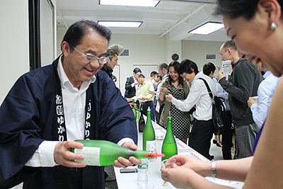 日本酒を注ぐ山本さん（左）。会場には笑顔があふれた（photo: Yuriko Anzai / 本紙）